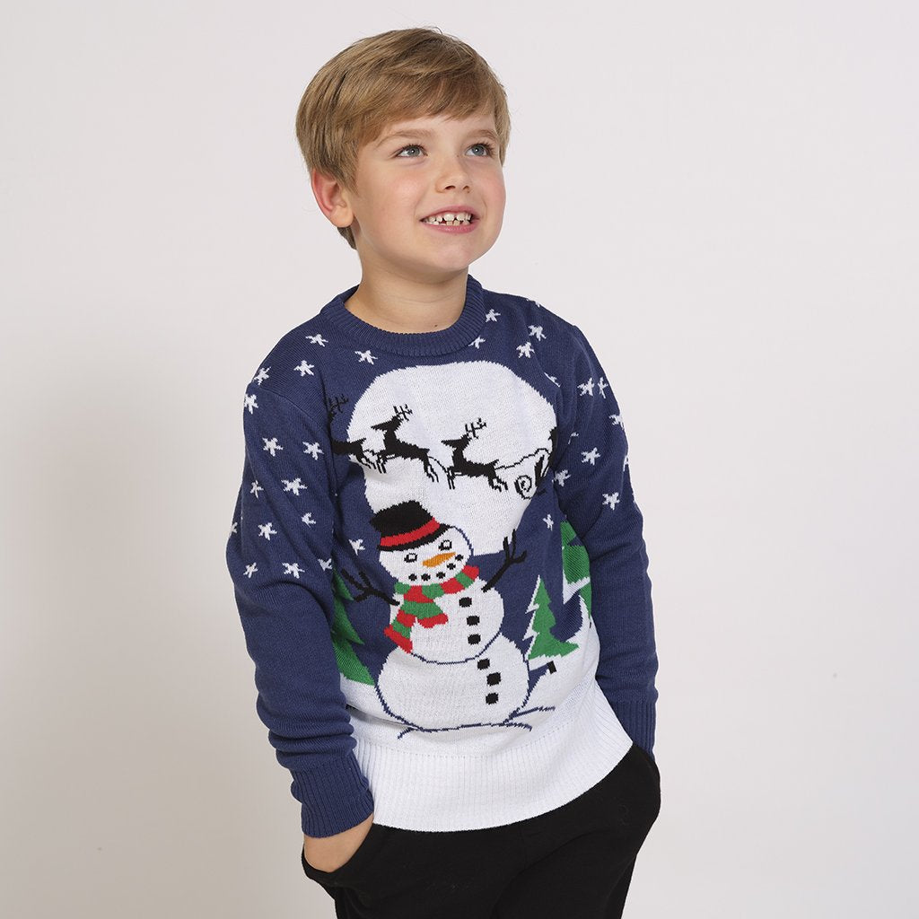 Ein Kind in einem blauen Weihnachtspulli mit einem Schneemann und einem Mond darauf.